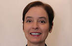 White woman with short, dark auburn hair and brown eyes looking forward towards the camera smiling.