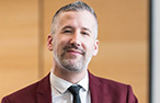 A whie man with grey hair and goatee wearing a red jacket.