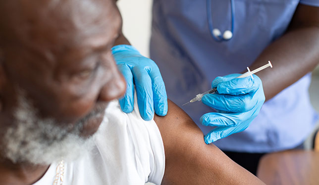 A black man receiving a vaccine from a black nurse.