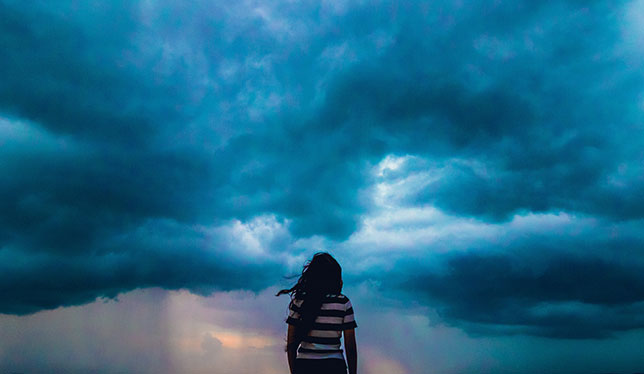 Une jeune femme de dos qui regarde une tempête.