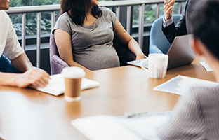 A pregnant woman sitting at table with some men.