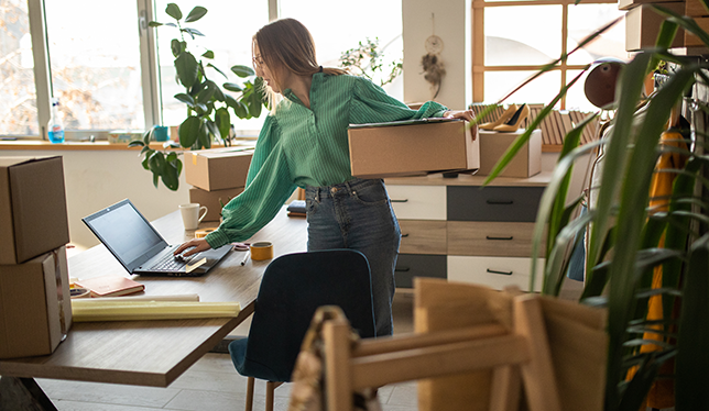 woman holding a box working on a laptop.