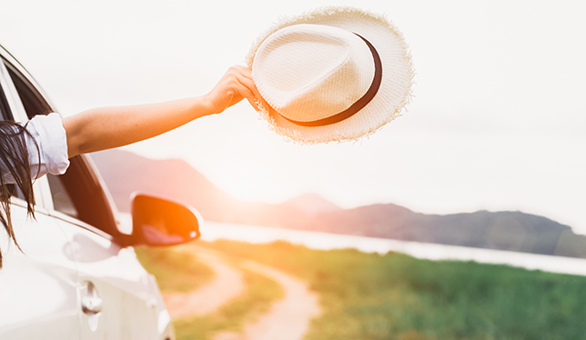 Le bras d'une femme tenant un chapeau qui sort par la fenêtre d'une auto.