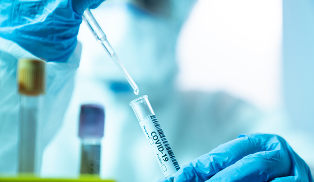 Close up photo of female scientist holding a laboratory pipette and a blood sample tube for covid-19 in laboratory. She is wearing a protective suit, laboratory glasses, surgical mask and surgical gloves. Selective focus on tube. Shot with a full frame mirrorless camera.